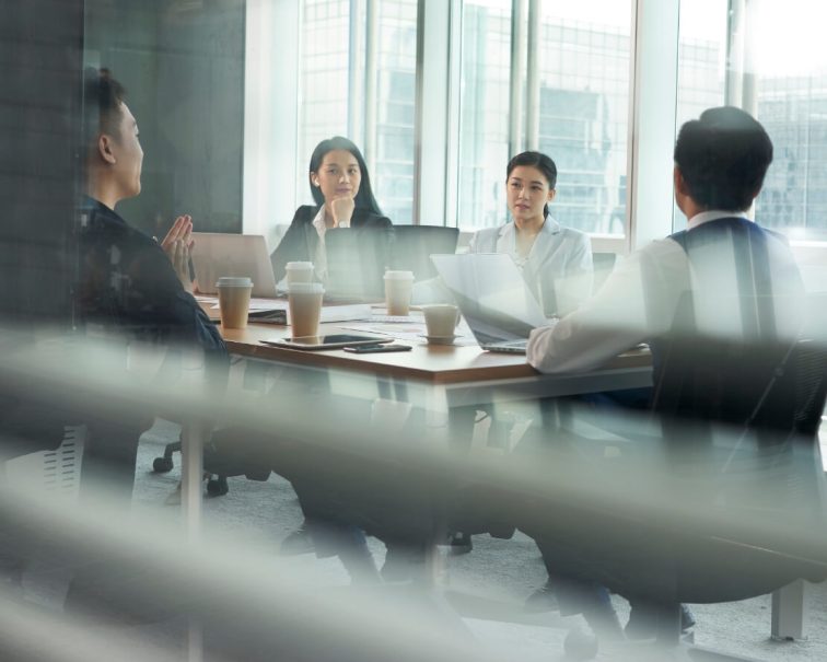 Business professionals in meeting around table with laptops and coffee cups in modern high-rise office