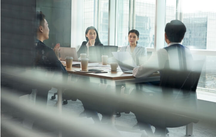 Business professionals in a modern office meeting room discussing strategy with laptops and coffee cups on the table