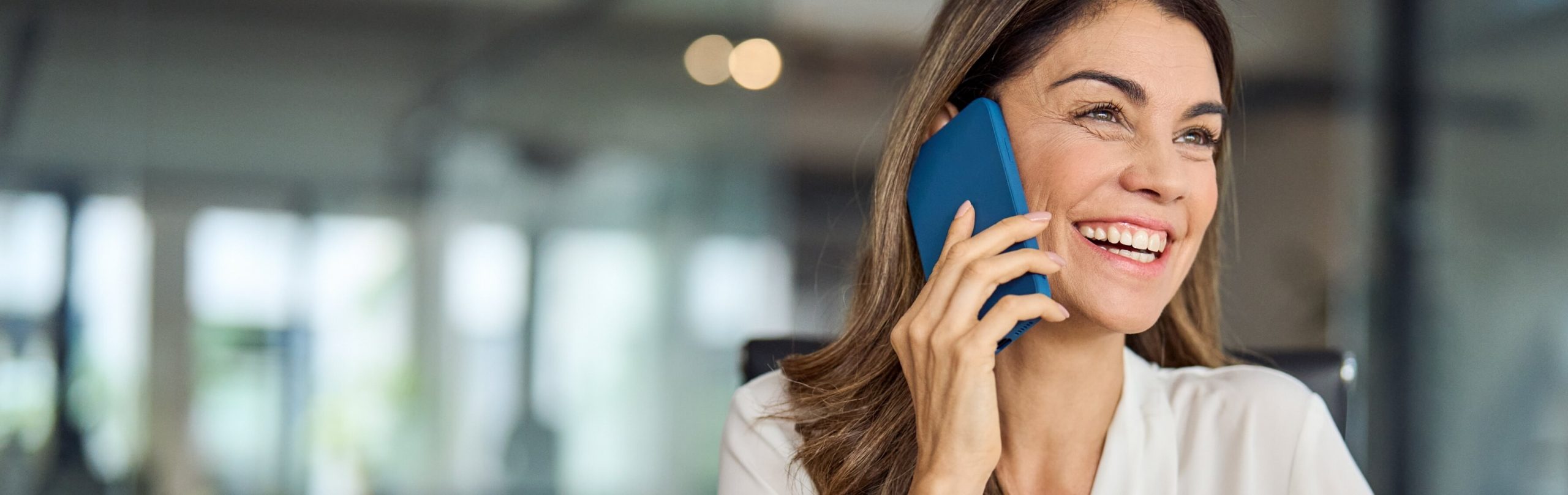 Professional woman smiling while speaking on blue phone in modern office setting