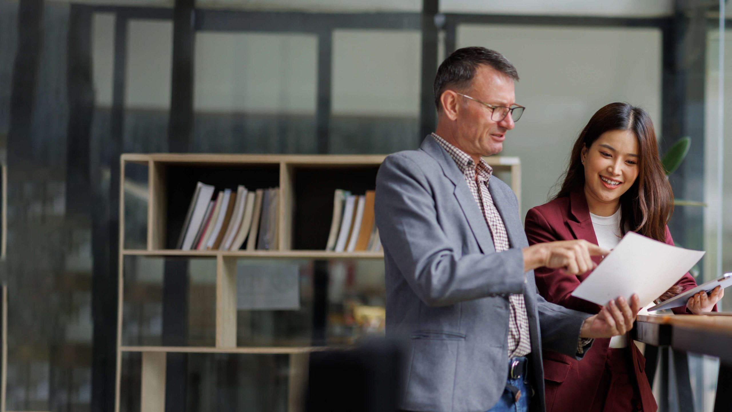 Two professionals reviewing documents in a modern office with shelving in the background