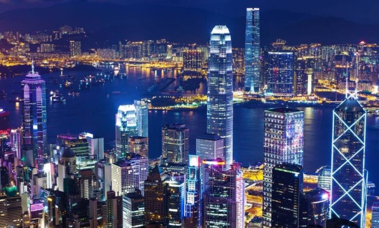 Illuminated nighttime cityscape of Hong Kong harbor with skyscrapers and Victoria Peak reflected in blue waters