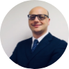 Professional headshot of a man wearing sunglasses and dark business suit against neutral background