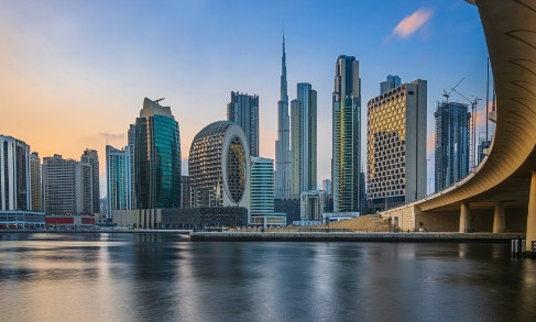 Dubai skyline with modern skyscrapers reflected in calm water at sunset, featuring iconic tower