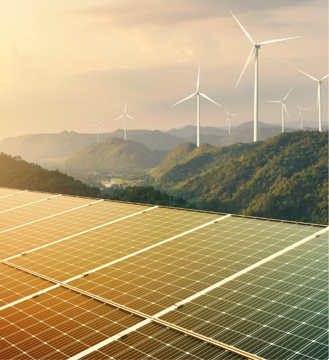 Solar panels in foreground with wind turbines on forested mountains at sunset, symbolizing renewable energy