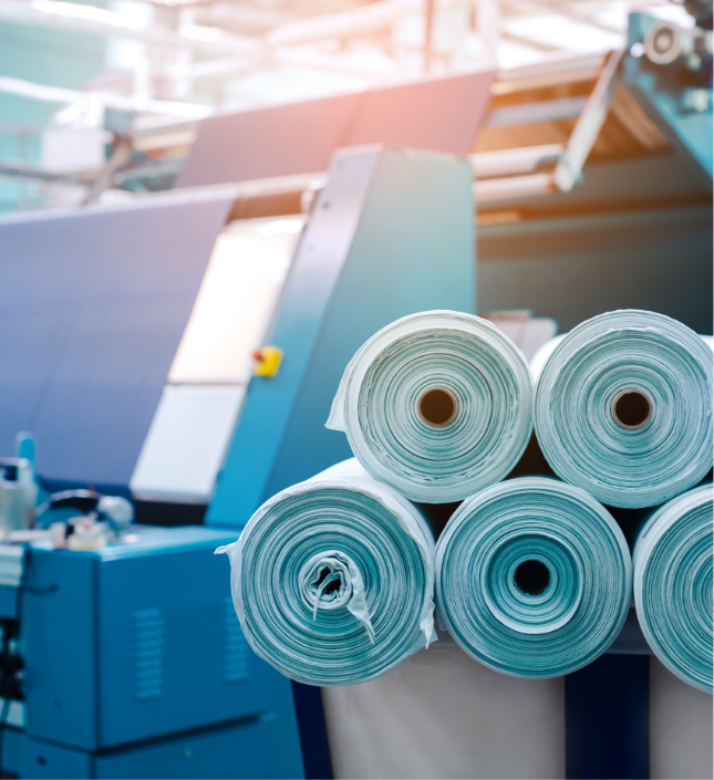 Rolls of turquoise fabric on industrial textile machinery in a manufacturing facility