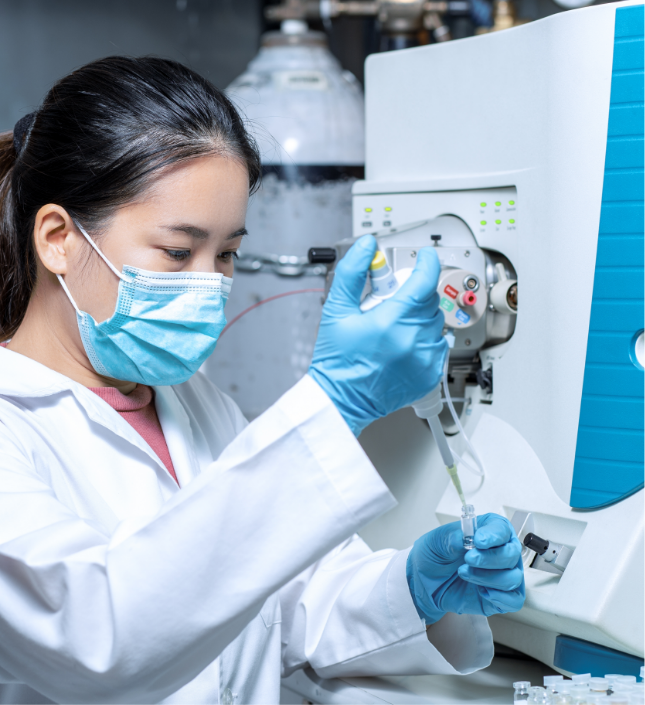 Female laboratory technician in white coat and blue gloves operating medical analysis equipment in a clinical setting