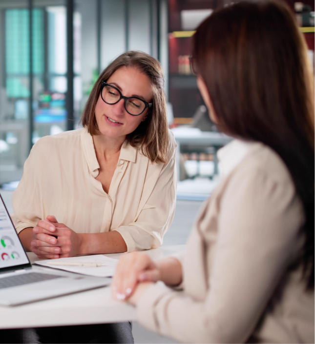 Two women in business attire having a discussion at a desk in a modern office setting