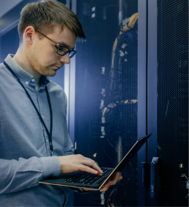 IT professional working on laptop in server room with data center infrastructure