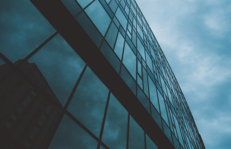 Modern glass and steel building facade against cloudy sky, representing corporate professional services
