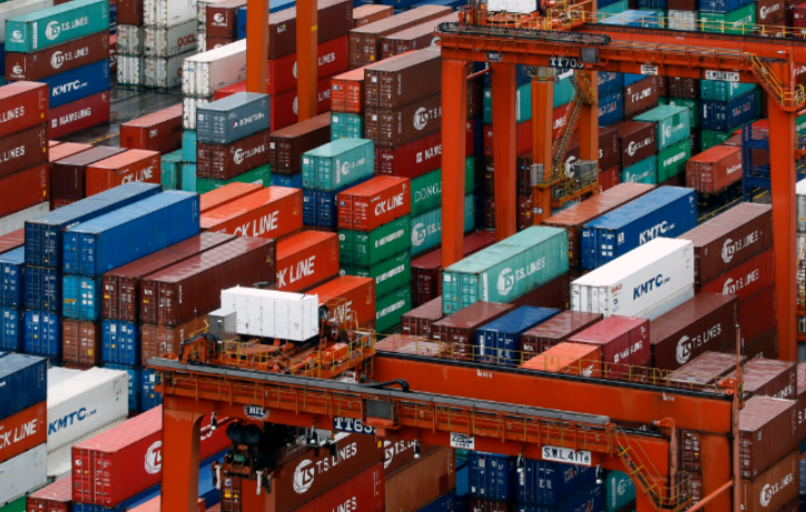 Stacked shipping containers in red, blue, and other colors at a cargo port with X-LINE and KMTC markings visible